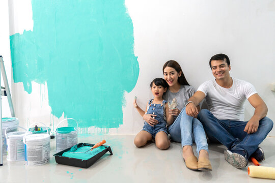Portrait of enjoy happy love asian family father and mother using a paint roller and painting walls, renovation, housework, diy, painting in their new home