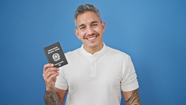 Young hispanic man smiling confident holding italian passport over isolated blue background