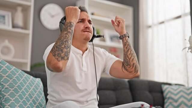 Young hispanic man playing video game sitting on sofa looking upset at home