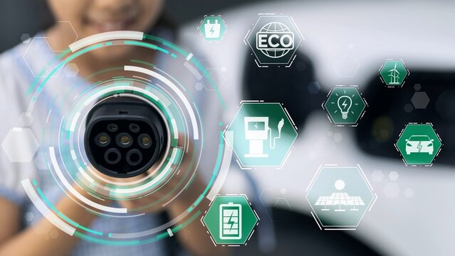 Focus young girl pointing EV charger in front of camera display eco-friendly pictogram hologram in blur background. EV car charger plug using alternative clean energy reducing CO2 emission.Peruse