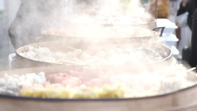 Steam rises slowmotion from the dimsum and dumplings of food in the traditional bamboo steamer