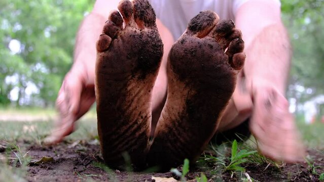 Close up of very dirty underfoot while rubbing soles with bare hands after walking through muddy ground. Man wearing white shirt and only black briefs.