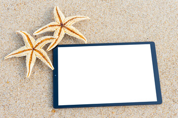 Starfishes on the sand of the beach and white screen of a tablet for copy space.  Template for ads for travel agencies. 