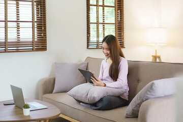 Women sitting on big sofa and writing notes on tablet with electronic pen in lifestyle at home