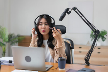 Female podcaster reading content on laptop and speaking on microphone to recording audio podcast