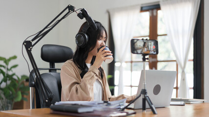 Female podcaster drinking coffee and writing note in paper while working to recording video podcast