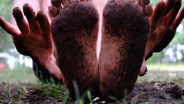 Close up of very dirty underfoot or soles and hands after doing gardening barefoot and without gloves.  Man wearing white shirt and only black briefs.