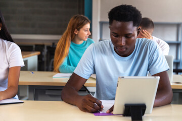 Teen black male student using digital tablet in class. African American high school student doing homework.Copy space.