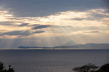 夕方の海に雲間から御光のように差し込む夕日。錦江湾パノラマパークから見る開聞岳