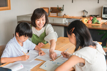 家で夏休みの宿題を手伝う母親と勉強する子供達
