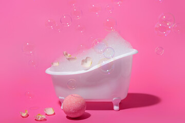 Small bathtub with foam, soap bubbles, flower petals and bath bomb on color background