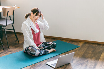 家のリビングでノートパソコンを使いながらヨガをするアジア人女性（困る・悩む）  © buritora