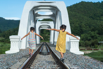 Children playing outside on train tracks. Asian sisters walking on the railway in rural scene.