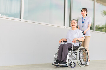 Fototapeta na wymiar 病院・介護施設で散歩する車椅子に乗った高齢者と介護士（ヘルパー・理学療法士・コピースペース） 