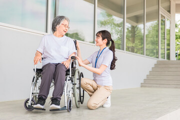 Fototapeta na wymiar 病院・介護施設で散歩中に話す車椅子に乗った高齢者と介護士（ヘルパー・理学療法士・コピースペース） 