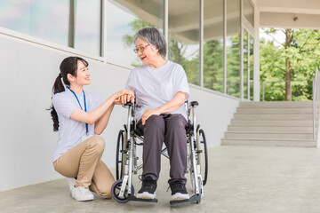 Fototapeta na wymiar 病院・介護施設で散歩しながら話す車椅子に乗った高齢者と介護士（ヘルパー・理学療法士） 