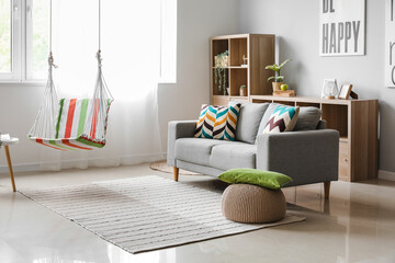 Interior of stylish living room with striped hammock and grey sofa