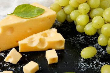 Board with tasty Swiss cheese and grapes on table