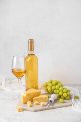 Board with tasty Swiss cheese, glass and bottle of wine on light background