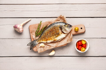 Board with tasty grilled dorado fish on light wooden background