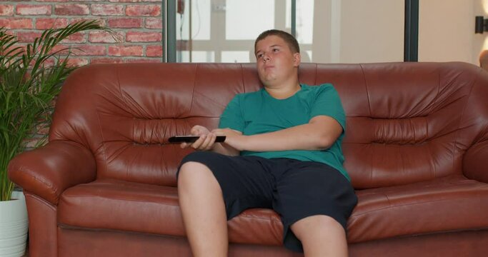 overweight handsome teenage boy lying on a sofa watching tv, kid resting at home slow motion free spare time leisure