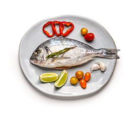 Plate of raw dorado fish with lemon and vegetables on white background