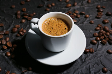 Cup of hot espresso and coffee beans on black background