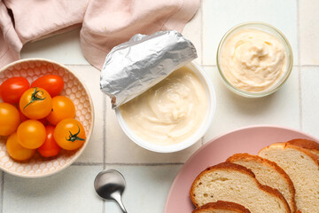 Plastic container and bowl of tasty cream cheese and tomatoes on white tile background