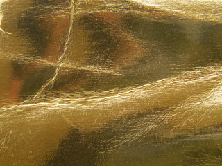 Close-up of golden and crumpled paper, grunge background and light reflection.