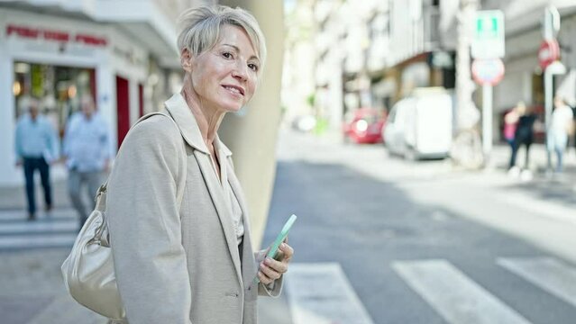 Middle age blonde woman using smartphone asking for taxi at street