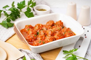 Baking dish of tasty meat balls with tomato sauce and parsley on white background