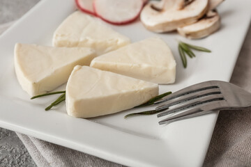 Plate with triangles of tasty processed cheese and vegetables on grey background, closeup