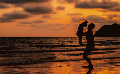 Silhouette of father throwing up his happy daughter in the air at sunset on tropical beach. Man and her child playing together outdoors on a sea.