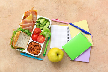 Stationery and lunch box with tasty food on grunge orange background