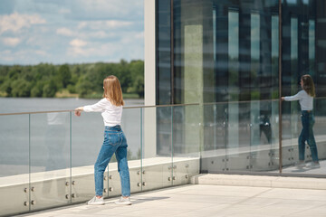 Woman stands on observation deck leaning on glass railing and looks at water