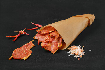 Dried pork jerky slices in parchment paper bag with salt and chilli pepper.