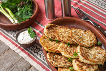 Plate of tasty zucchini fritters with sour cream on wooden background