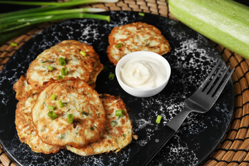 Board of tasty zucchini fritters with sour cream on table