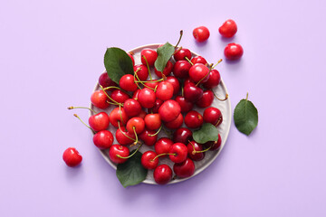 Plate of sweet cherries and leaves on lilac background