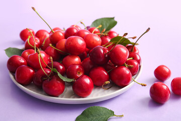 Plate of sweet cherries and leaves on lilac background