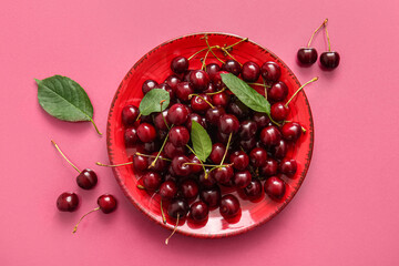 Plate of sweet cherries and leaves on pink background