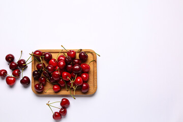 Wooden board with sweet cherries on white background