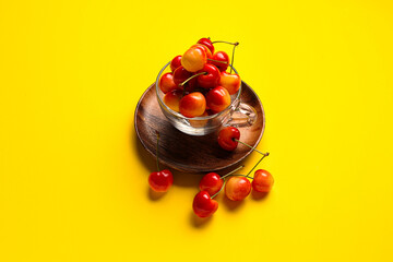 Glass cup with sweet cherries on yellow background