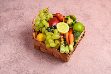 Wicker basket with different fresh fruits and vegetables on pink background