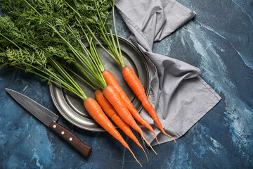 Plate of fresh carrots with leaves on blue background