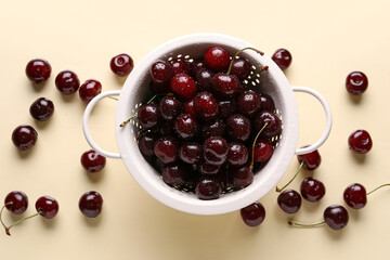 Colander with sweet cherries on beige background