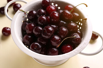 Colander with sweet cherries on beige background