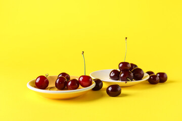 Plates with sweet cherries on yellow background