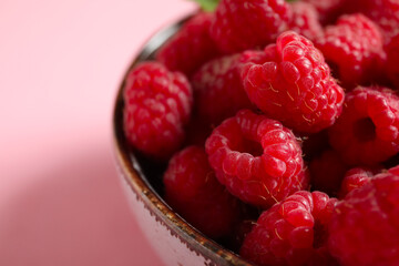 Bowl with fresh raspberries on pink background