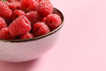 Bowl with fresh raspberries on pink background